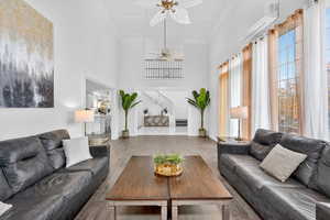Living room featuring ornamental molding, a wall unit AC, wood finished floors, a towering ceiling, and a ceiling fan