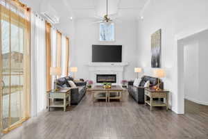 Living area with a ceiling fan, a towering ceiling, a glass covered fireplace, wood finished floors, and ornamental molding
