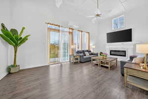Living room with a glass covered fireplace, dark wood-type flooring, ceiling fan, and a high ceiling