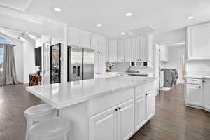 Kitchen featuring white cabinets, recessed lighting, dark wood-type flooring, stainless steel refrigerator with ice dispenser, and a kitchen breakfast bar