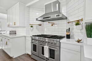 Kitchen with range with two ovens, white cabinetry, island range hood, tasteful backsplash, and dark wood-style floors