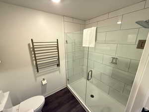 Full bath featuring a shower stall, dark wood-style floors, radiator, and a towel warming rack