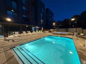 Pool at night with a community pool, a patio, and a hot tub