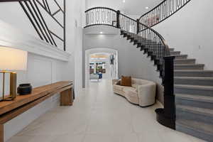 Tiled foyer entrance with stairs, a towering ceiling, and arched walkways