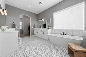 Bathroom featuring vanity, a soaking tub, tile walls, and recessed lighting