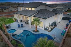 Back of property at dusk featuring a patio area, an in-ground hot tub, and a fenced backyard