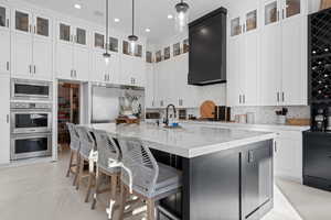 Kitchen featuring light stone counters, white cabinets, built in appliances, a kitchen island with sink, and recessed lighting