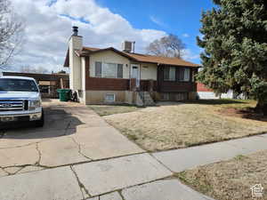 View of front of house featuring a chimney, a front yard, and concrete driveway