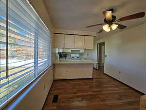 Kitchen with a peninsula, dark wood-type flooring, electric stove, white cabinetry, and ceiling fan