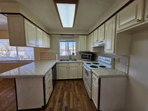 Kitchen with tile counters, appliances with stainless steel finishes, dark wood finished floors, a textured ceiling, and under cabinet range hood
