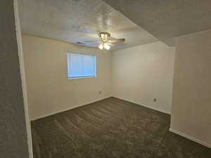 Basement Bedroom featuring a textured wall, a textured ceiling, dark carpet, and a ceiling fan