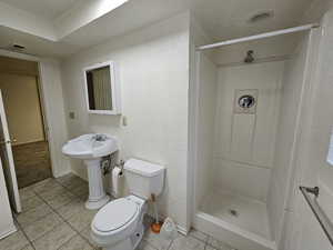 Basement 3/4 Bathroom featuring light tile patterned floors, a textured wall, a textured ceiling, and a shower stall