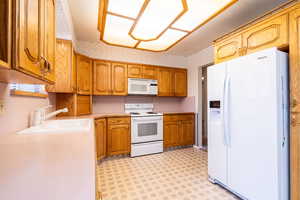 Kitchen featuring white appliances, wallpapered walls, light countertops, light flooring, and brown cabinets