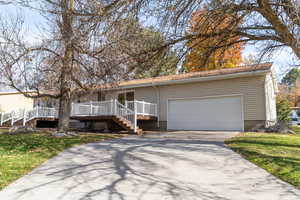 Ranch-style house featuring concrete driveway, a back yard, an attached garage, and a deck