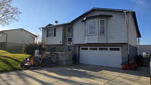 Split foyer home featuring concrete driveway, aluminum siding/brick, an attached garage, and a front lawn