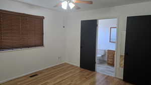 Primary bedroom featuring light wood finished floors, a ceiling fan, and ensuite bathroom