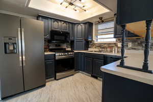 Kitchen featuring appliances with stainless steel finishes, a raised ceiling, light countertops and backsplash