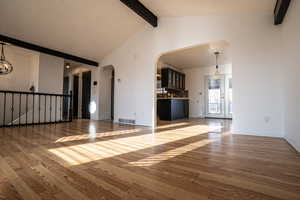 Unfurnished living room featuring hardwood / wood-style flooring, beam ceiling, arched walkways, and high vaulted ceiling