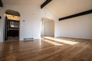Unfurnished room with beamed ceiling, dark wood finished floors, arched walkways, and high vaulted ceiling