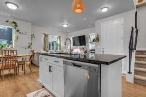 Kitchen featuring stainless steel dishwasher, open floor plan, light wood-style flooring, and white cabinetry