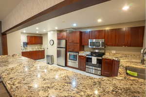Community Kitchen with a peninsula, dark brown cabinets, recessed lighting, appliances with stainless steel finishes, and light stone counters