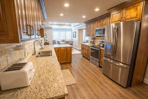 Kitchen featuring tasteful backsplash, a raised ceiling, stainless steel appliances, light stone countertops, and a peninsula