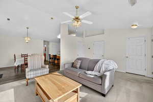 Living room with lofted ceiling, light colored carpet, a ceiling fan, and a chandelier