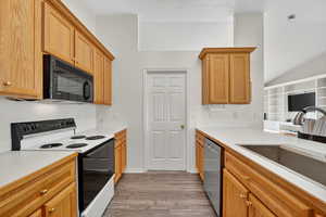 Kitchen featuring range with electric cooktop, light countertops, light wood-type flooring, black microwave, and lofted ceiling