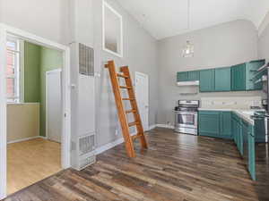 Kitchen featuring dark wood-type flooring, light countertops, a heating unit, appliances with stainless steel finishes, and high vaulted ceiling