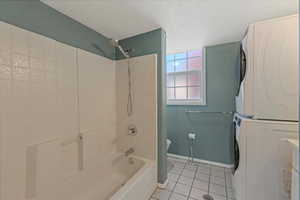 Bathroom with light tile patterned floors, bathtub / shower combination, vanity, estacked washer and dryer, and a textured ceiling