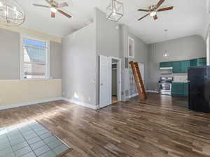 Unfurnished living room featuring ceiling fan, dark wood finished floors, a towering ceiling, and a wainscoted wall