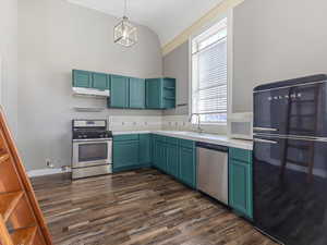 Kitchen with appliances with stainless steel finishes, open shelves, dark wood-type flooring, hanging light fixtures, and vaulted ceiling