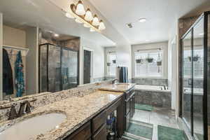 Full bath featuring a walk in closet, double vanity, a bath, a textured ceiling, and a shower stall