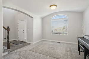 Foyer entrance featuring stairway, arched walkways, carpet floors, and vaulted ceiling