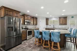 Kitchen featuring stainless steel appliances, a breakfast bar, light stone counters, dark brown cabinetry, and a center island