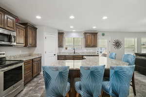 Kitchen featuring appliances with stainless steel finishes, a kitchen bar, light stone countertops, healthy amount of natural light, and recessed lighting