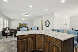 Kitchen featuring dark brown cabinetry, recessed lighting, open floor plan, light stone counters, and a kitchen island