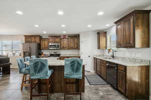 Kitchen featuring recessed lighting, dark brown cabinets, light stone countertops, a center island, and stainless steel appliances