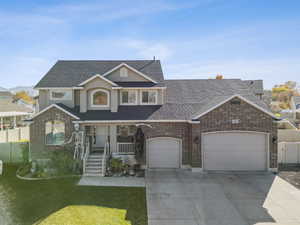 View of front of property featuring a porch, brick siding, driveway, and roof with shingles