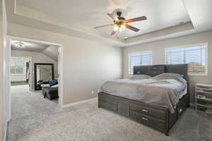 Bedroom featuring a raised ceiling, light colored carpet, ceiling fan, and a textured ceiling