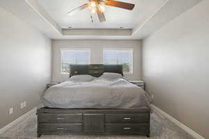 Carpeted bedroom featuring a raised ceiling, a textured ceiling, and a ceiling fan