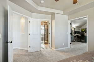 Unfurnished bedroom with light colored carpet, a desk, ceiling fan, a raised ceiling, and ensuite bathroom