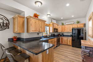 Kitchen with black appliances, light wood-type flooring, recessed lighting, a peninsula, and light brown cabinetry