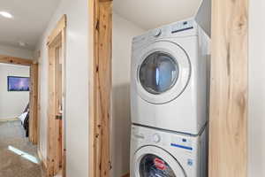 Washroom featuring stacked washer and clothes dryer and carpet flooring