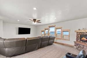 Carpeted living room with a stone fireplace, recessed lighting, and a ceiling fan