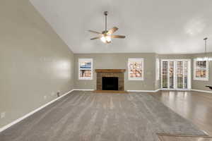 Unfurnished living room featuring a fireplace with raised hearth, lofted ceiling, a ceiling fan, carpet flooring, and wood finished floors