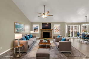 Living room featuring a stone fireplace, ceiling fan, high vaulted ceiling, wood finished floors, and a chandelier