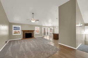 Unfurnished living room featuring a fireplace, high vaulted ceiling, dark wood-type flooring, and ceiling fan