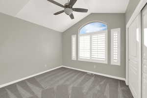 Unfurnished bedroom with vaulted ceiling, dark carpet, and a ceiling fan