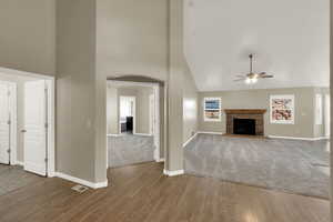 Unfurnished living room with high vaulted ceiling, wood finished floors, a brick fireplace, arched walkways, and a ceiling fan